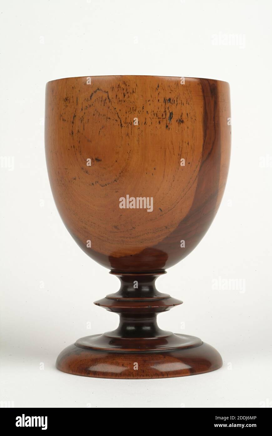 Cup, Goblet, 1700-1800, Made in England. This laburnum wood goblet is one of a pair, probably dating from the eighteenth century. We can tell that it was made on a pole lathe because the point where the goblet was held in place on the lathe leaves a characteristic mark on the base. It is very difficult to date these plain wooden goblets accurately as styles and patterns changed very slowly over the years. Laburnum wood was an interesting choice for this goblet as its warm tones and contrasting dark heart and yellow sapwood help to add a certain beauty and finesse Stock Photo