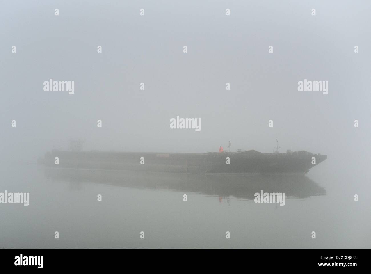orange gekleider Mann auf einem Schiff welches aus dem Nebel auftaucht Stock Photo