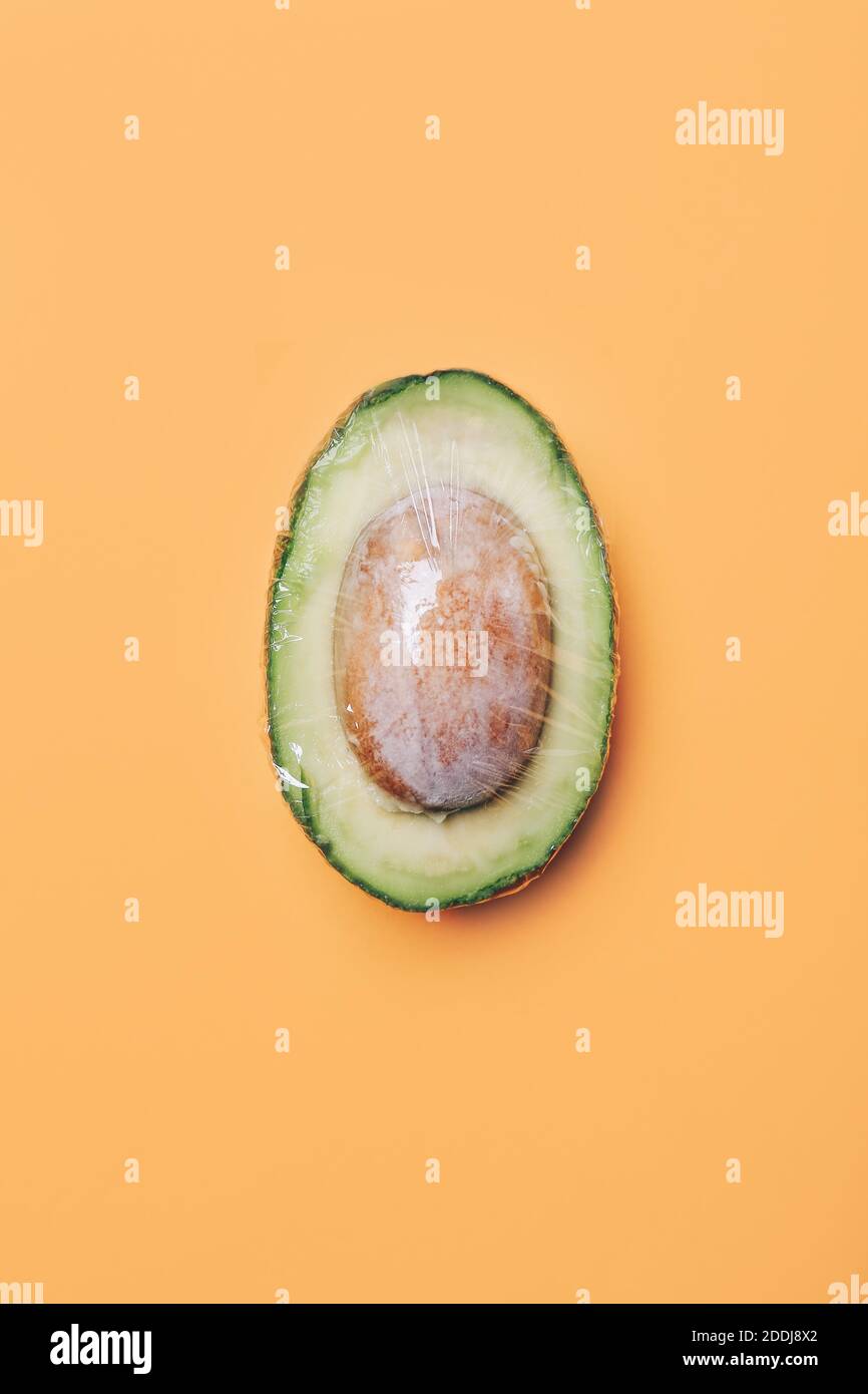 Avocado in wrap polyethylene plastic on colored background. Minimal enviromental concept. Flat flat, top view Stock Photo