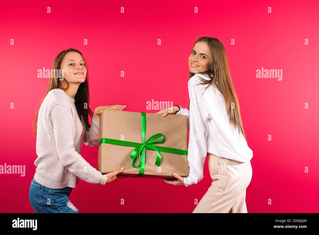 Beautiful girls posing with big gift box on a pink background. Holiday concept. Stock Photo