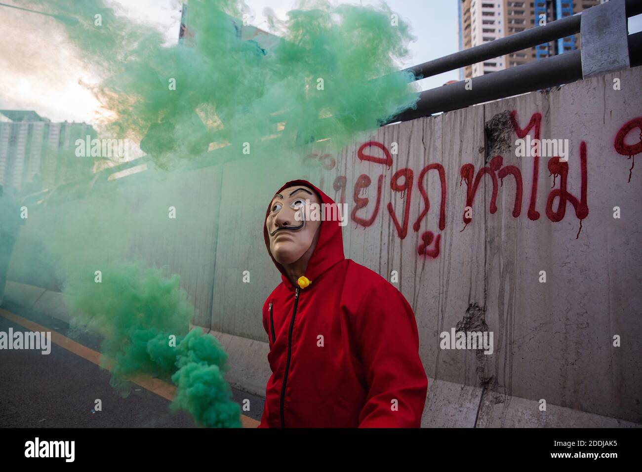 A protester wearing an anonymous mask holds a burning flare during the demonstration.Thousands of pro-democracy protesters gathered outside the headquarters of Siam Commercial Bank (SBC) to demand Thailand's King Maha Vajiralongkorn to give the royal assets to the people. The pro-democracy protesters also call for the resignation of Thailand Prime Minister and the reform of the monarchy. Stock Photo