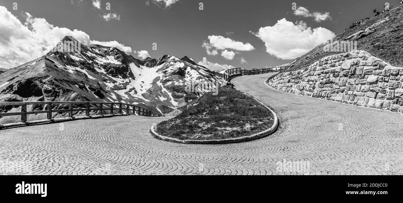 Mountain cobbled road serpentine. Sharp curve with mountain tops on background. High Tauern, Austria. Black and white image. Stock Photo