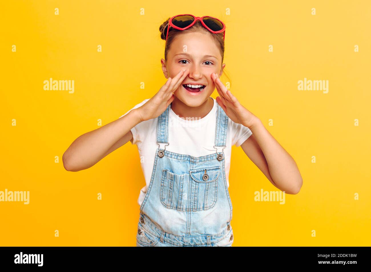 Portrait of a happy teenager, shocked girl screaming good news at camera, standing on yellow background Stock Photo