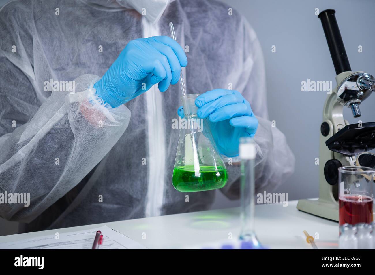 Technician in protective clothing hand stirring and shaking green