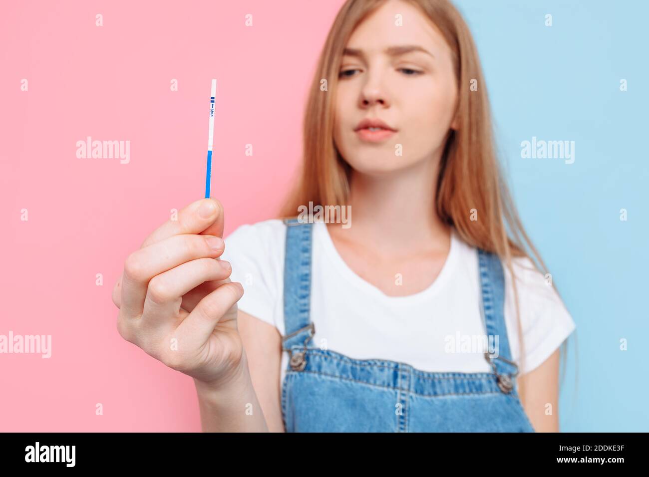 Yes, I'm pregnant A happy beautiful young pregnant woman shows a positive result of two strips on the test, standing on an isolated pink and blue back Stock Photo