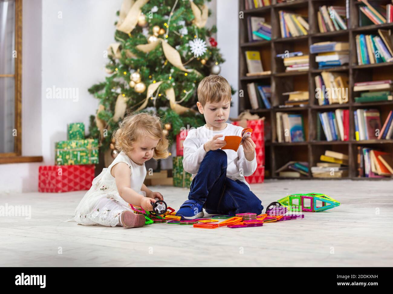 Young girl and boy playing with magnetic toys beside Christmas tree at home Stock Photo