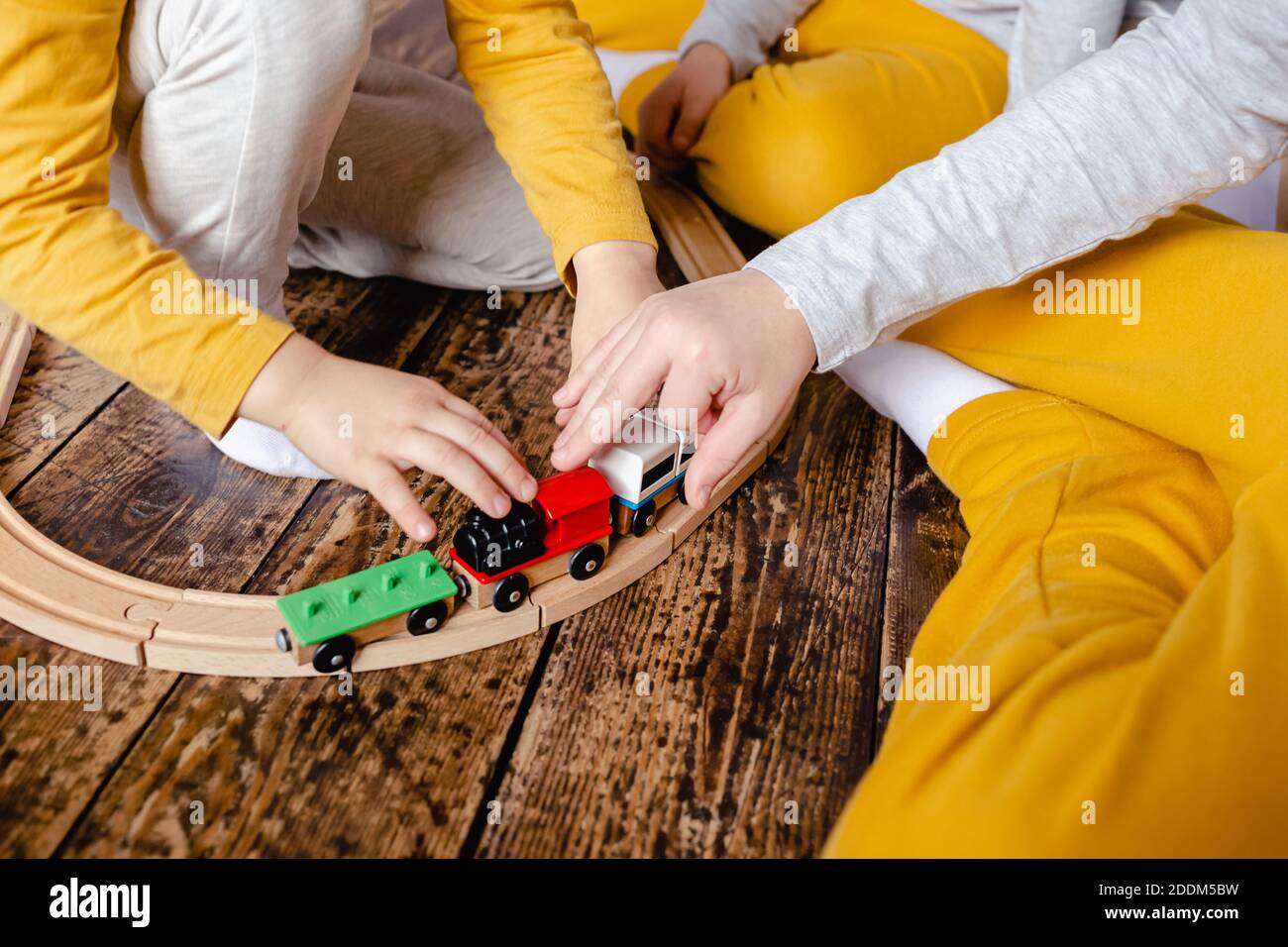 Toddler boys building railway and playing with wooden train sitting on floor at living room. Little boys playing with a toy car. Kids play. Stock Photo