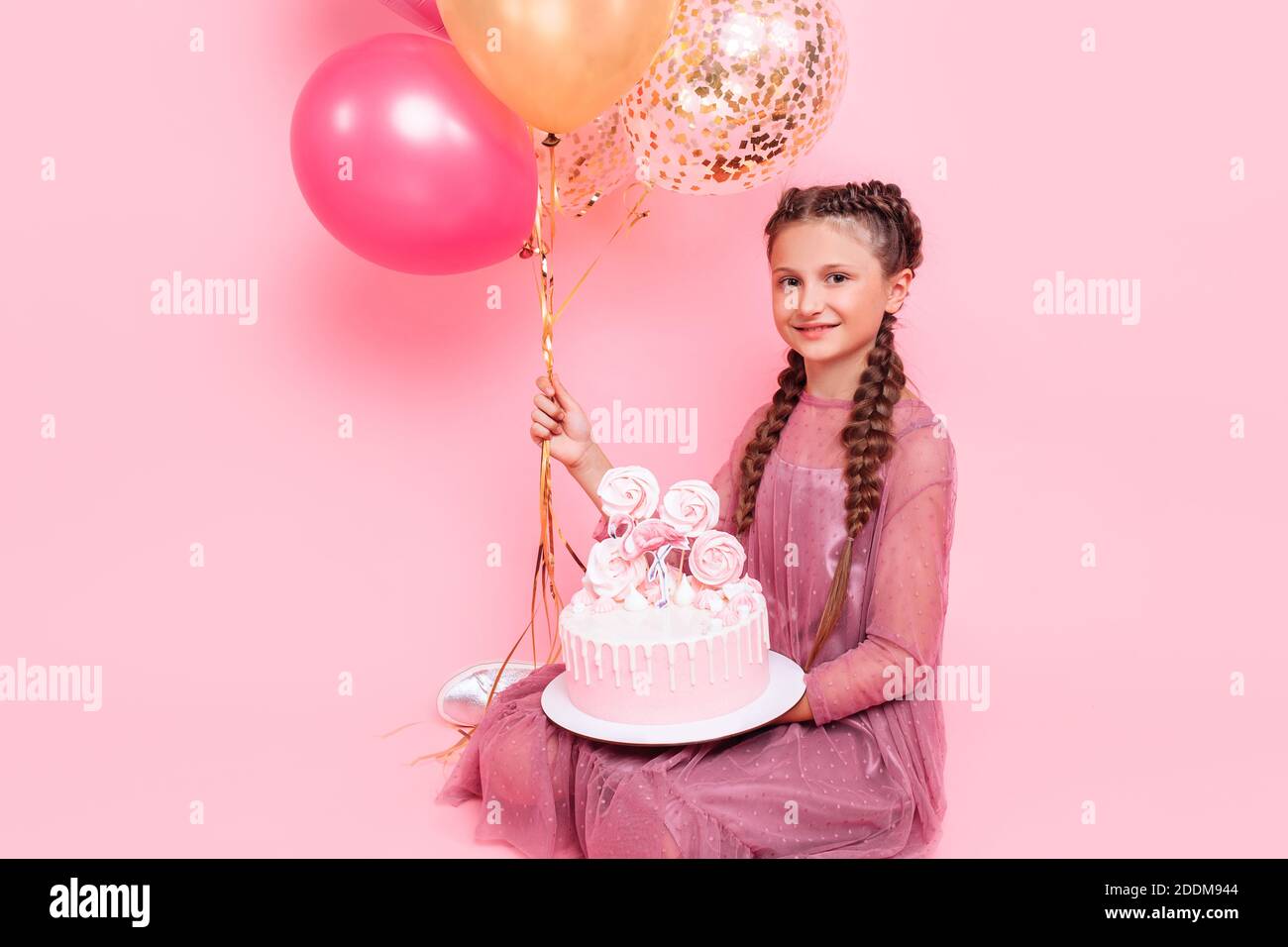 A teenage girl with balloons holds a cake in her hands, on a pink