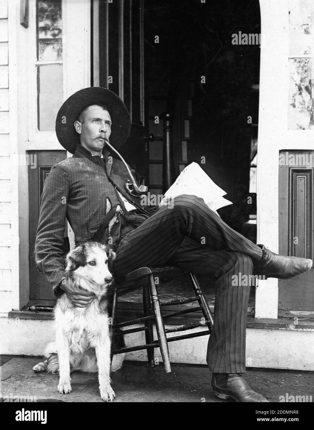 Probably in the 1880s, this laidback young man, perhaps in his 30s, sits on his back-tilted chair, with his right hand on his pet dog. He seems to be thinking about something relaxing. Taking a break from reading his newspaper, the man is smoking a curved, long-stemmed pipe that has a figure (maybe a monkey) carved below the tobacco bowl.   To see my other homey-related images, Search:  Prestor  vintage  home  [or  pet] Stock Photo