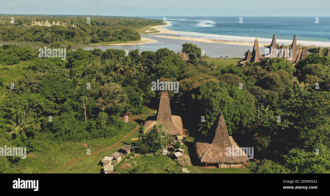 Indonesia long-held tradition village with ornate roof at sand beach aerial view. Extraordinary houses, bees hives at green valley with tropic forest. Amazing nature landscape of Sumba Island, Asia Stock Photo