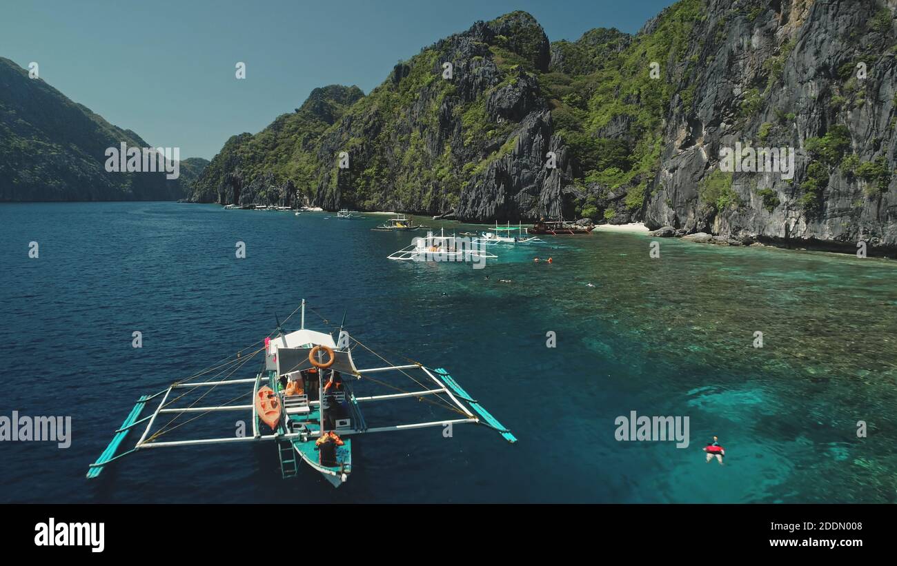 Serene tropical nature scape at mountain island of Palawan, Philippines, Visayas Archipelago. Closeup passengers boats at ocean coast with cliff shore at summer tour. Cinematic close up drone shot Stock Photo