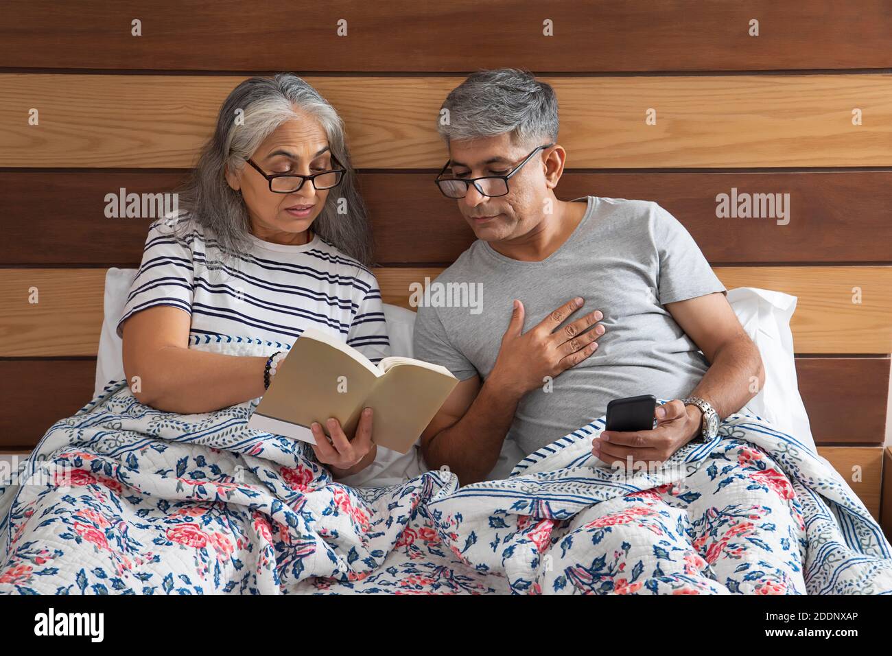 elderly couple sitting in bed reading and exchanging notes Stock Photo