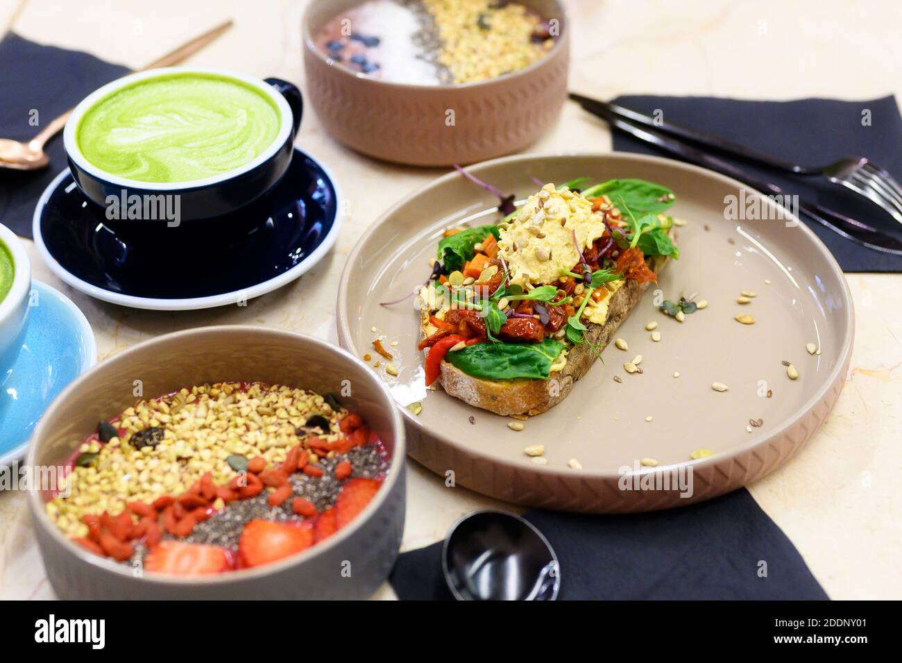 raw healthy food breakfast. smoothie bowl, toast with hummus, and matcha latte green tea cup on the table Stock Photo