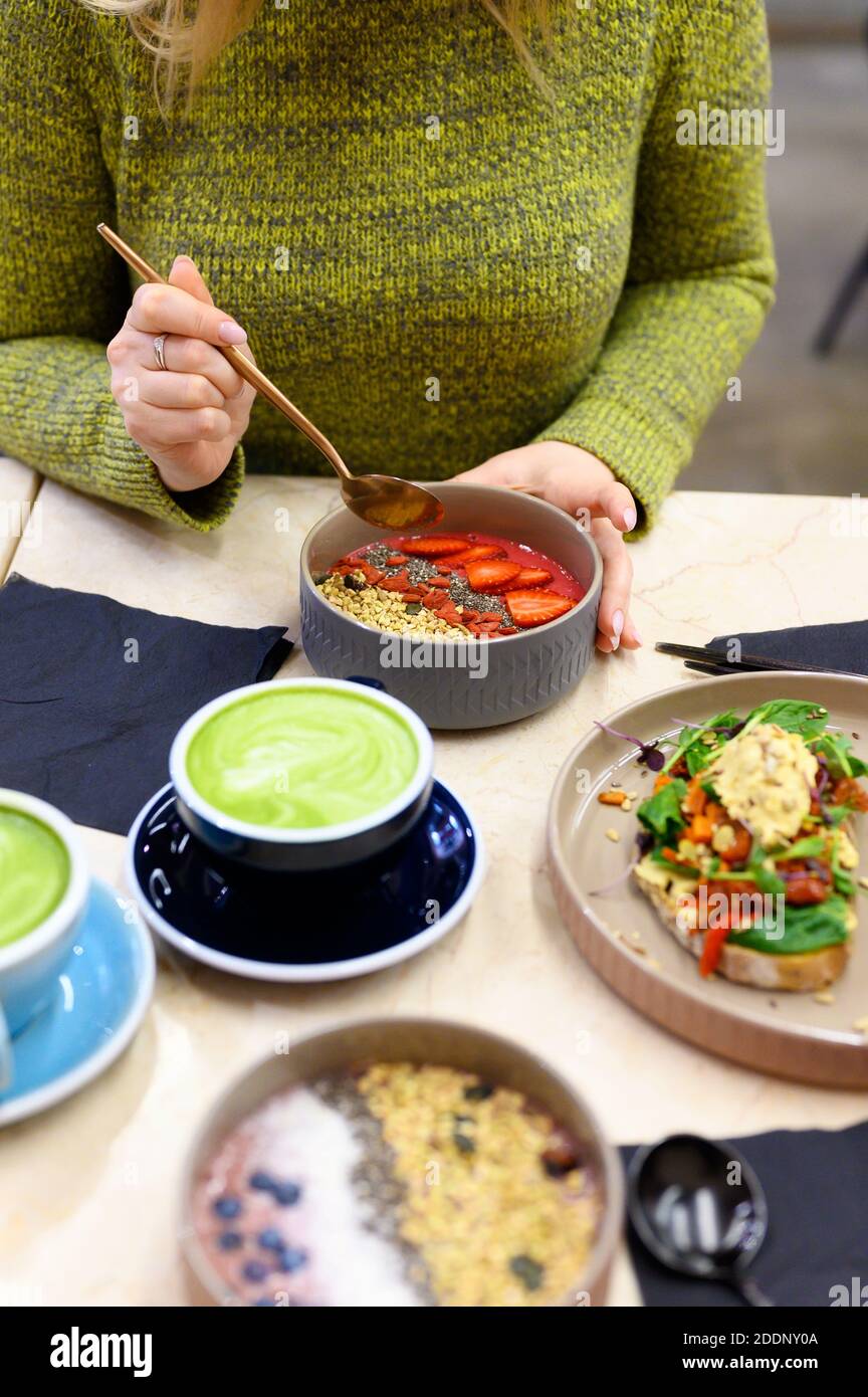 raw healthy food breakfast and woman, ready to eats. smoothie bowl, toast with hummus, and matcha latte green tea cup on the table. vertical photo Stock Photo