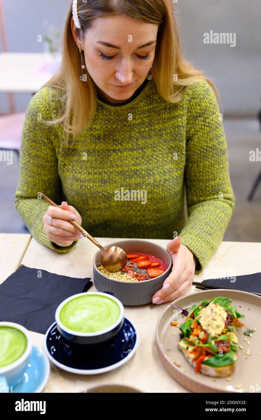 raw healthy food breakfast and woman, ready to eats. smoothie bowl, toast with hummus, and matcha latte green tea cup on the table. vertical photo Stock Photo