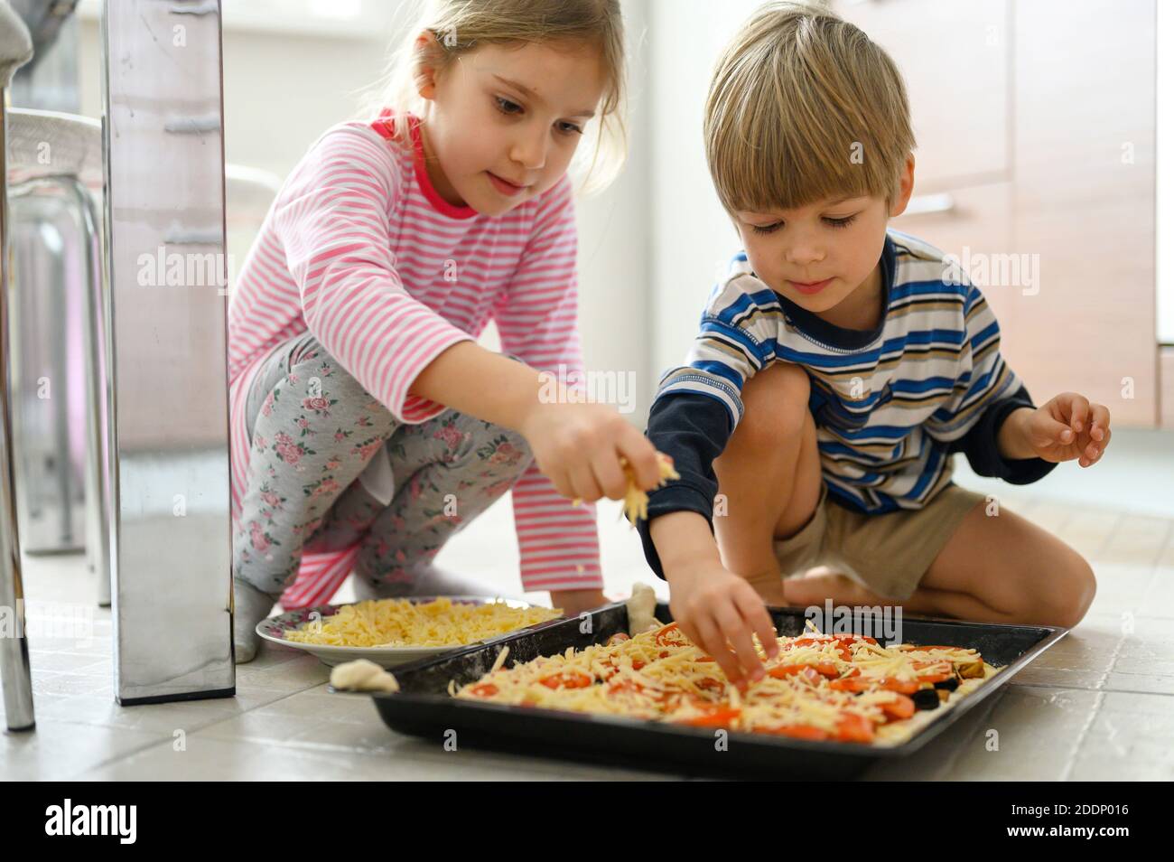happy family make food at home. little kids son and daughter helps his mother cooking pizza in the kitchen. concept pastimes of isolation time in quar Stock Photo