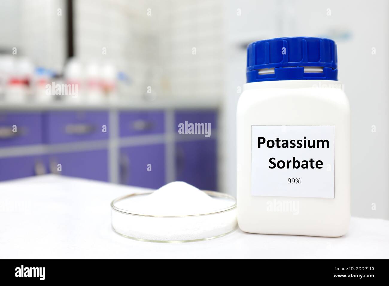Selective focus of bottle of pure potassium sorbate food additive beside a petri dish with white solid powder substance. White laboratory background. Stock Photo