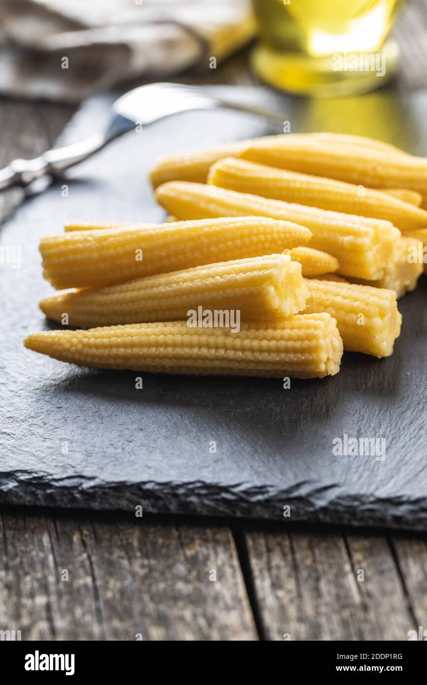 Pickled young baby corn cobs on a black stone cutting board. Stock Photo