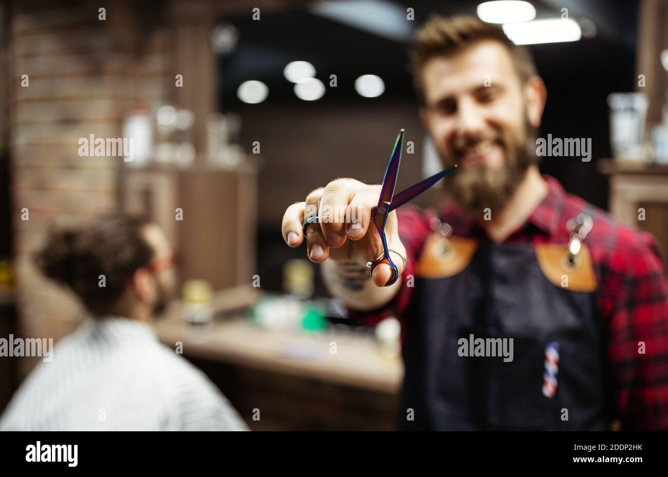 Portrait of happy young barber with client at barbershop and smiling. Stock Photo