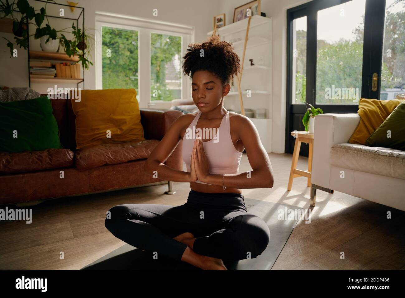 Young african woman sitting in lotus position with joined hands on yoga mat practicing breathing exercise Stock Photo