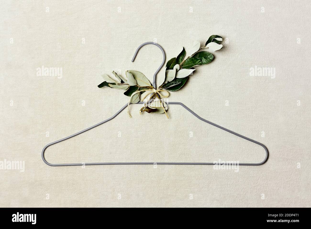 Iron hanger with sprig of the tree with leaves on linen background. Natural aestetic, Eco-friendly, Chic, Cozy, Sustainable Sale concept. Zero waste Stock Photo