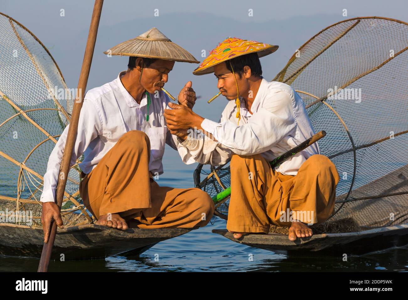 Intha leg rowing fishermen at Inle Lake, Myanmar (Burma), Asia in February - conical hats hat, having a rest and smoke, lighting smoking cigar cigars Stock Photo