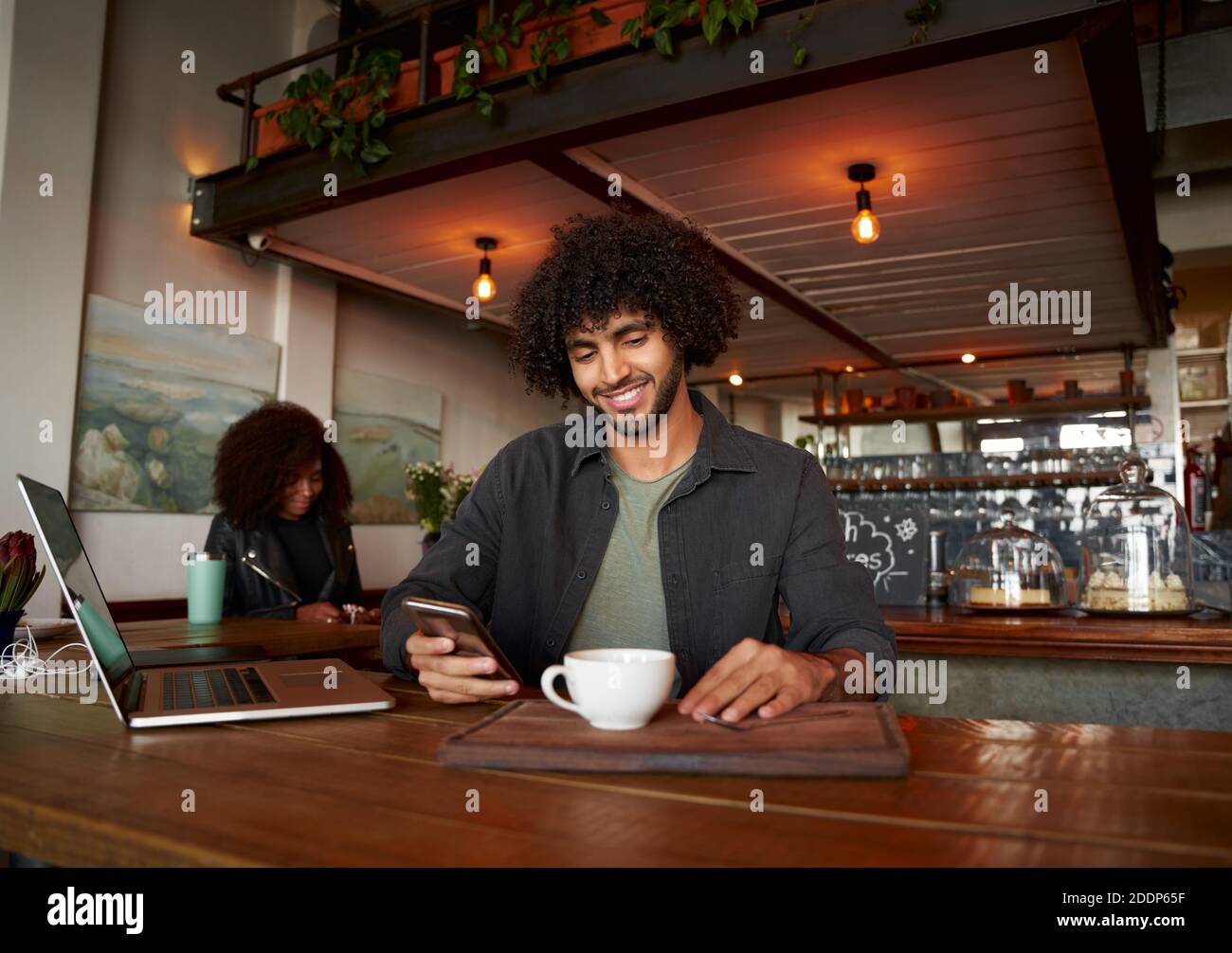Handsome young man using smartphone and laptop in modern cafe while drinking coffee Stock Photo