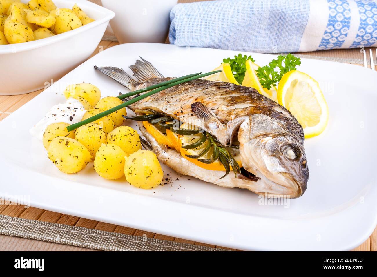 Grilled fish with potatoes, sauce, lemon and cutlery Stock Photo