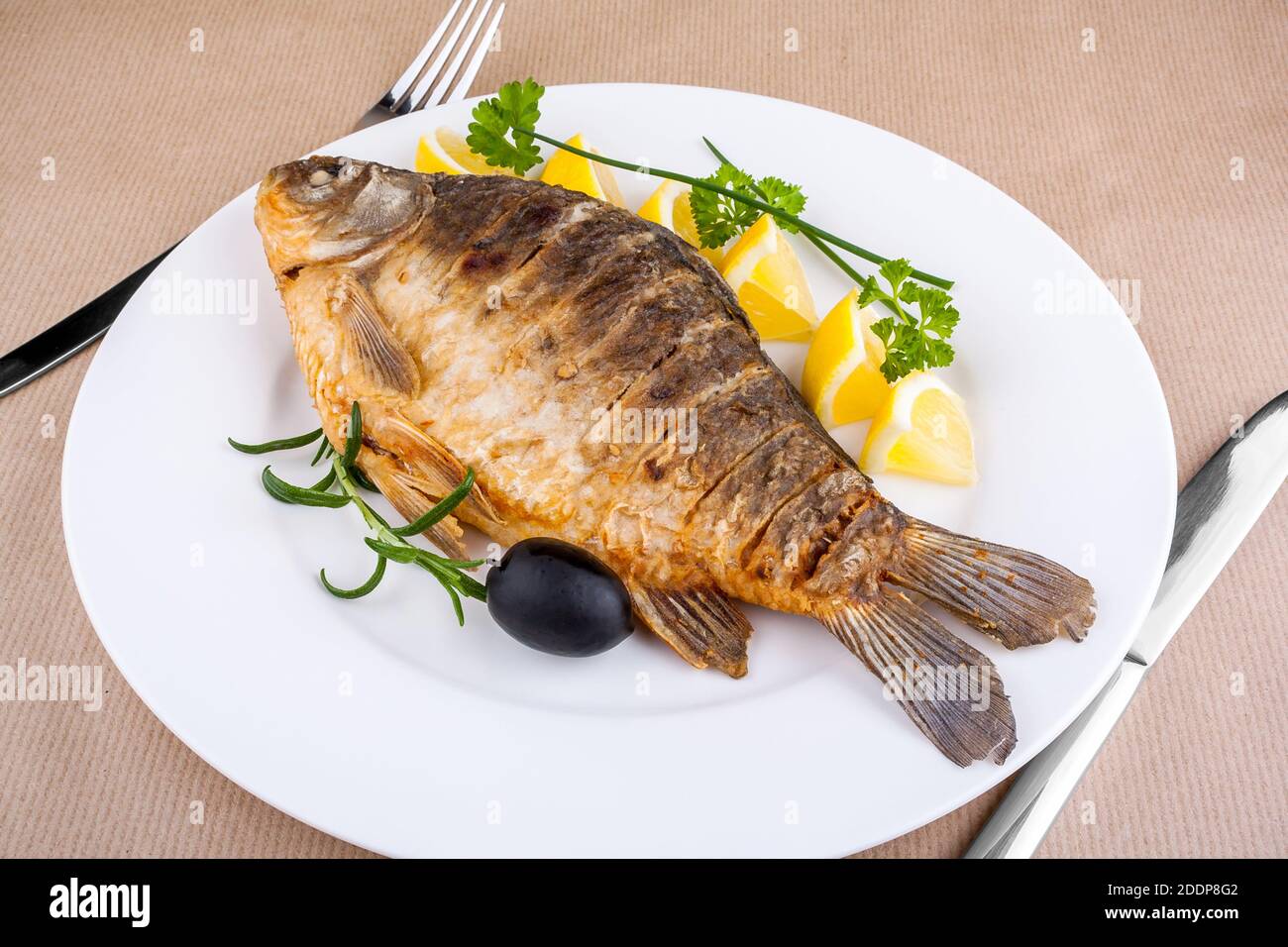 Fried fish on white plate with fork and knife, closeup Stock Photo