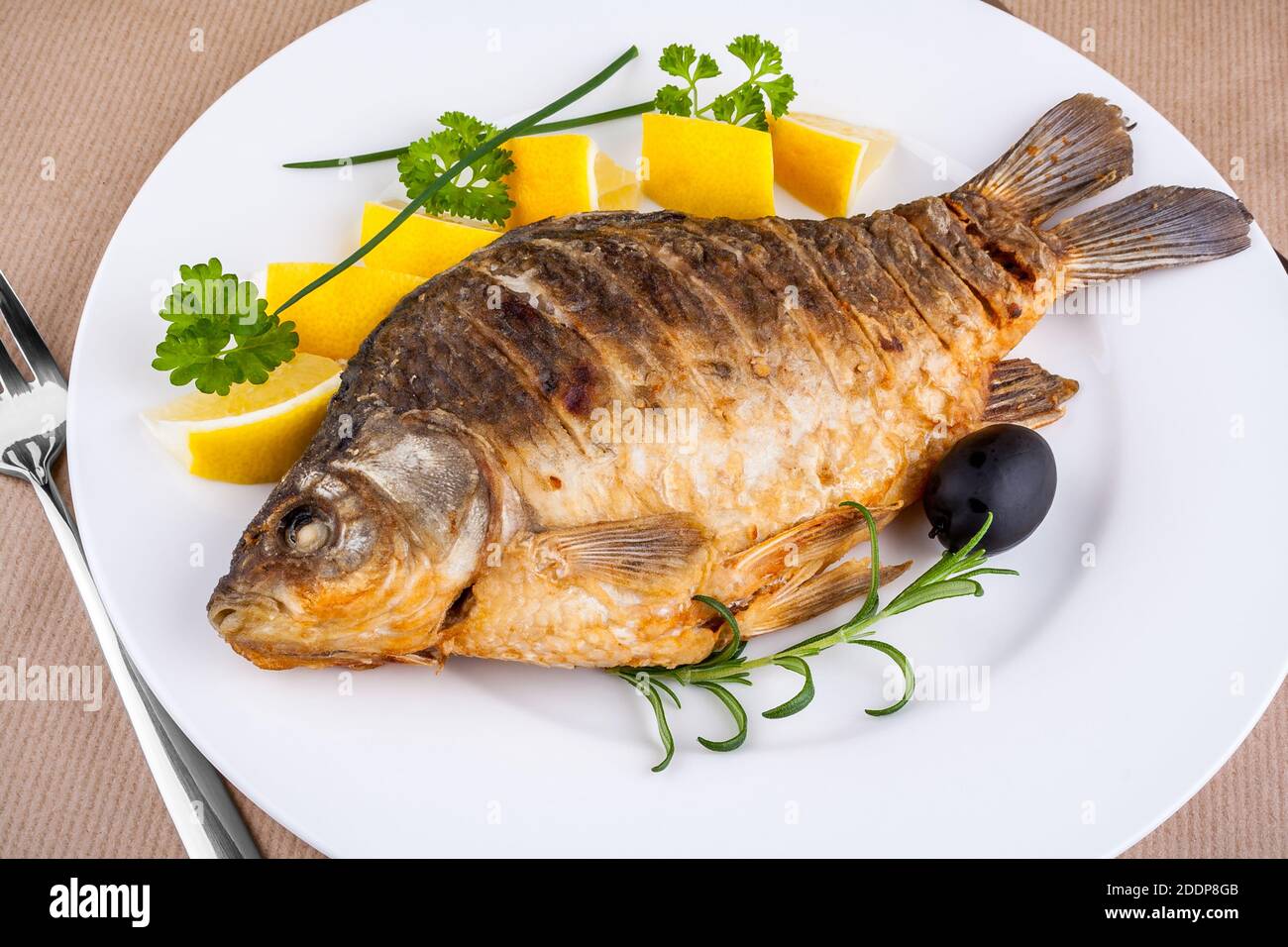 Fried fish on white plate with fork and knife, closeup Stock Photo