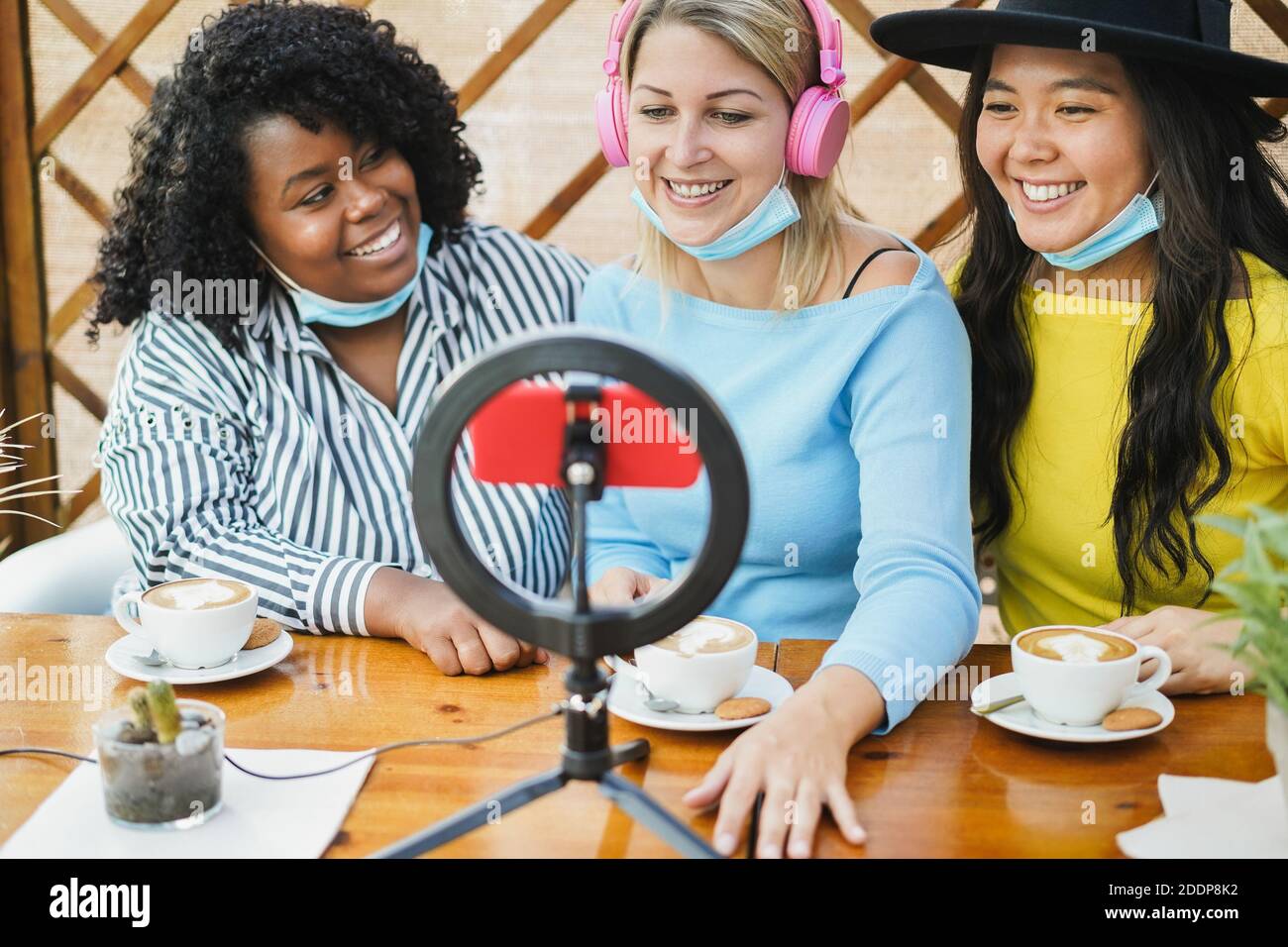 Multiracial girls streaming online using influencer led and phone cam during coronavirus outbreak - Young women wearing safety mask while having fun w Stock Photo