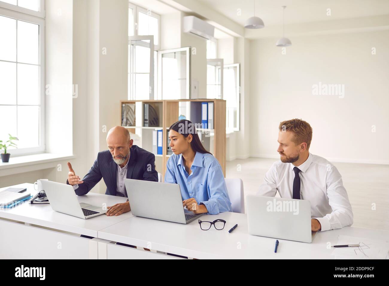 Serious mature company manager and young trainee employees working on laptops together Stock Photo