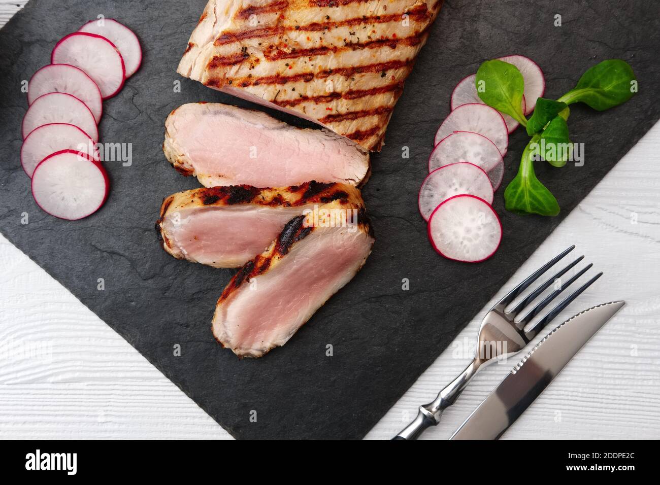 Sliced grilled pork fillet with fresh tomatoes and raddish served with glass of red wine. Stock Photo