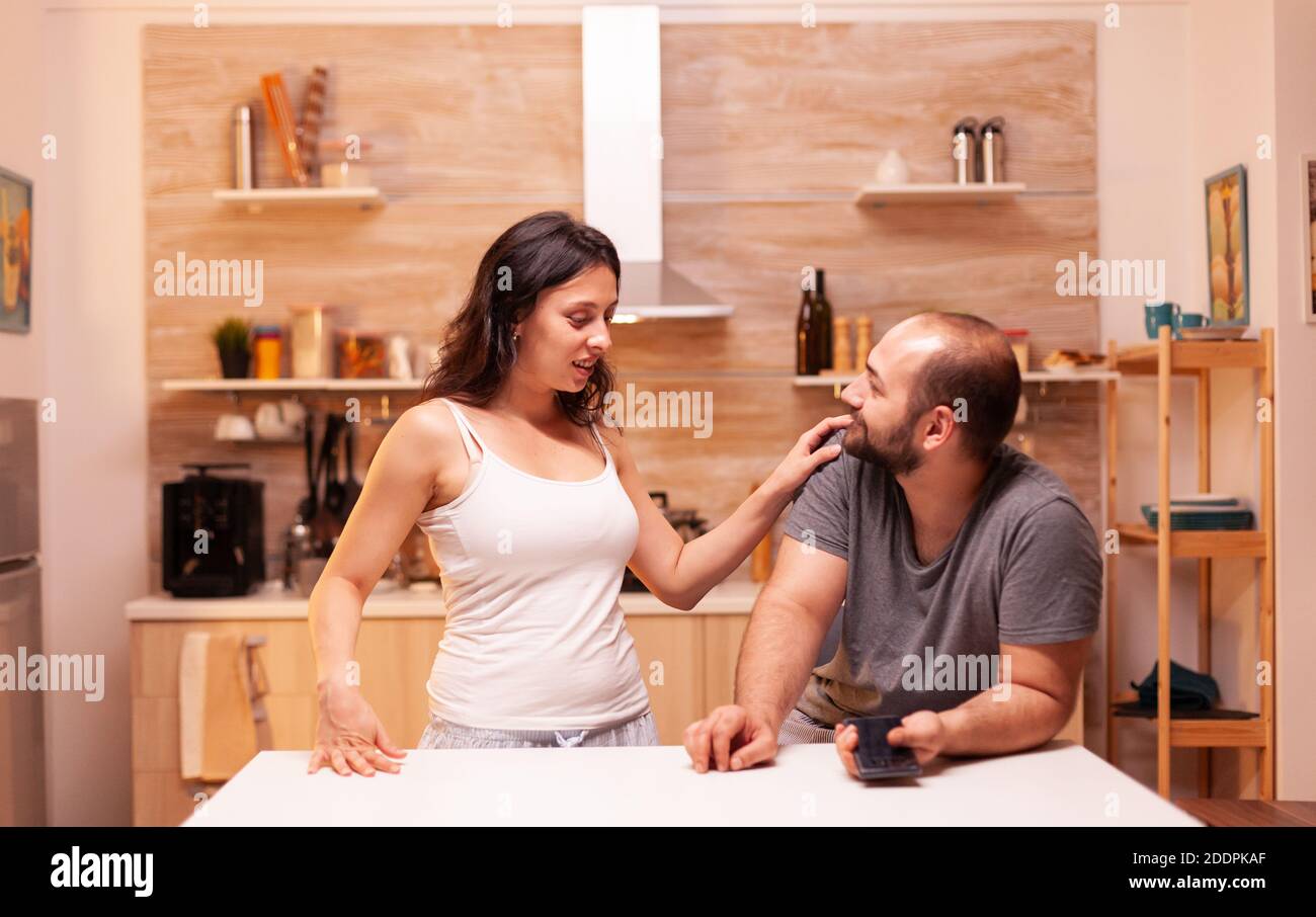 Wife suspecting husband of cheating while having a conversation with him in kitchen. Heated angry frustrated offended irritated accusing her man of infidelity showing him messages . Stock Photo