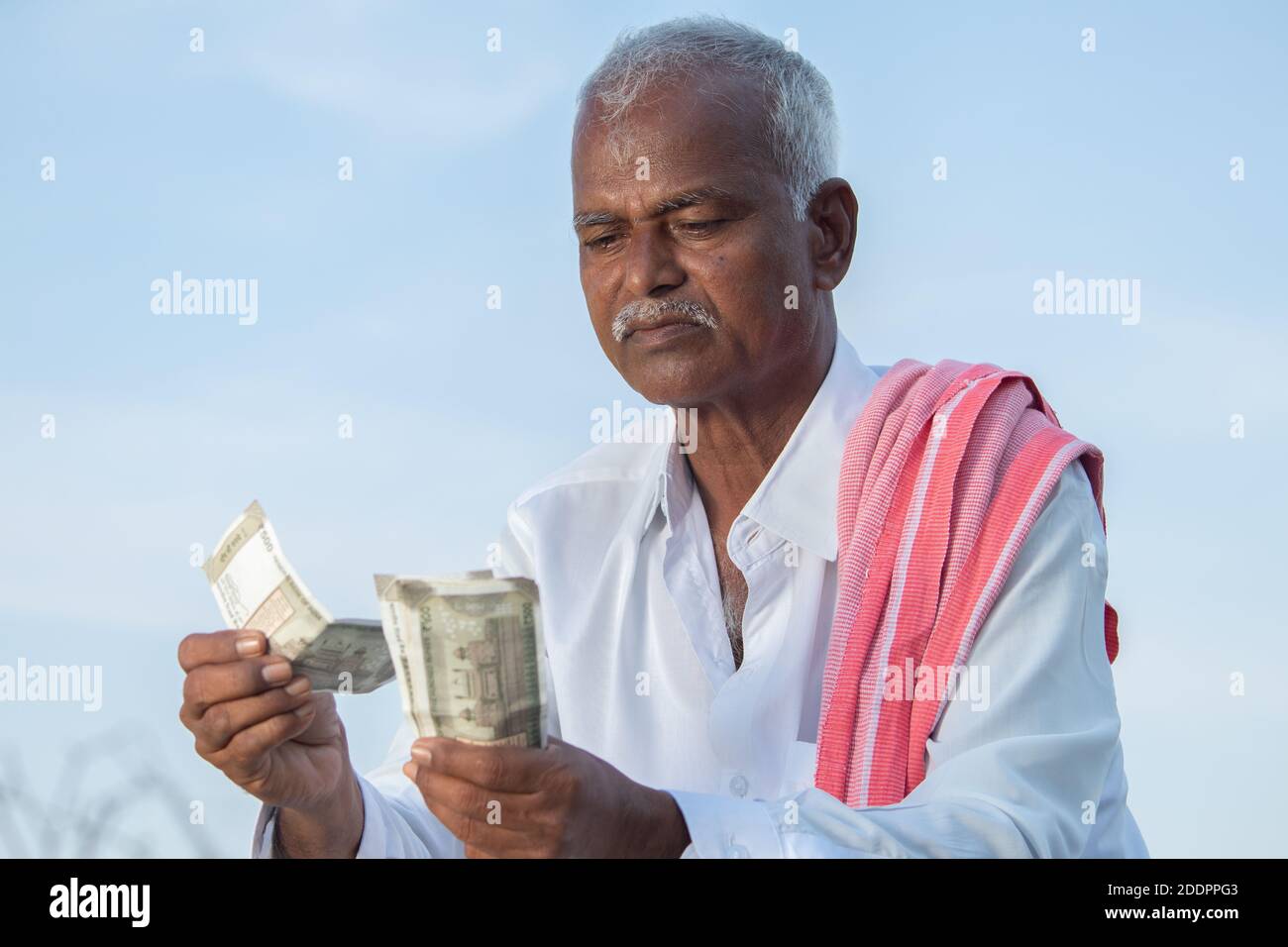 Indian Farmer angry about his income due to low crop yield, profit or loan repayment while counting money. Stock Photo