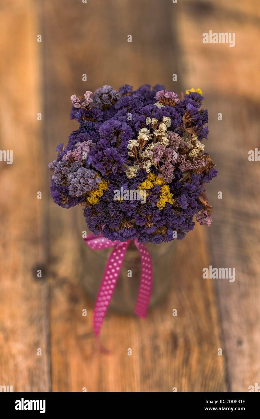 a bouquet of dried flowers, Limonium sinuatum, wavyleaf sea lavender, statice, notch leaf marsh rosemary, sea pink in a jar, pink ribbon, wooden floor Stock Photo