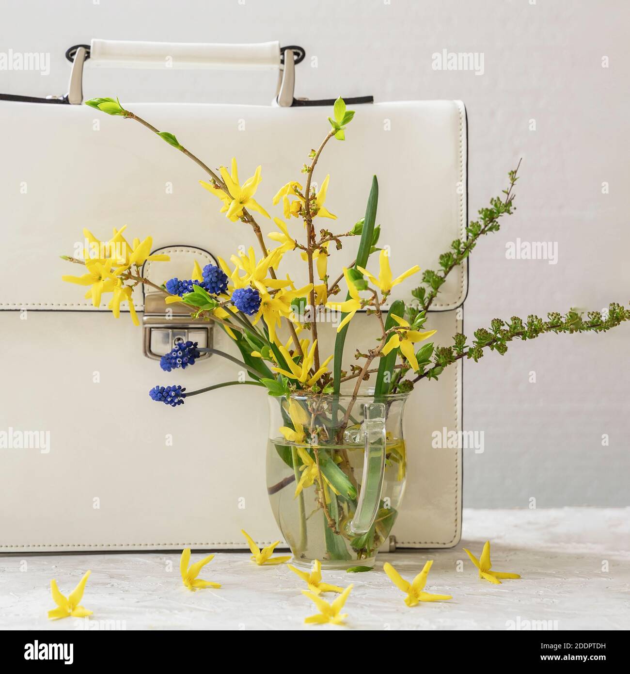 Bouquet of wild colorful flowers in glass vase and white briefcase, close-up. Concept of spring stilelife, seasonal shopping Stock Photo