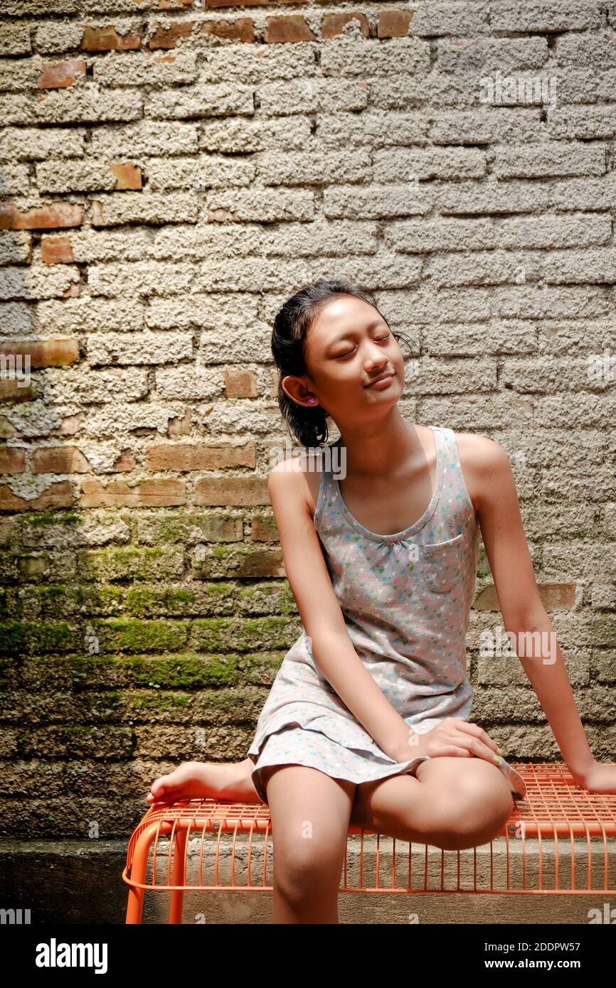 Southeast Asian ethnicity teenage girl sitting on a bench, happy sunbathing in the morning at home Stock Photo