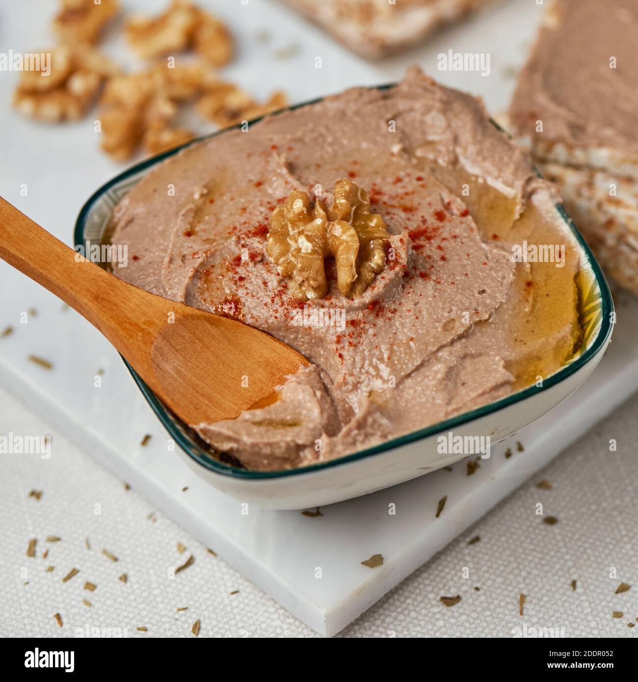 closeup of a bowl with an appetizing hummus, made with chickpea, walnut and rosemary, on a table, next to some puffed rice cakes Stock Photo