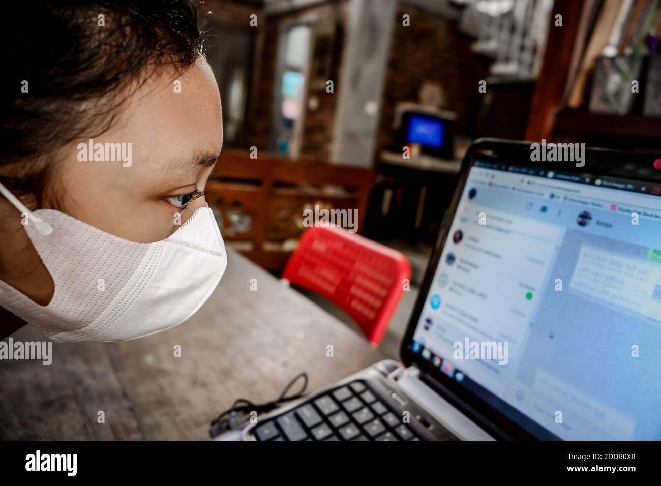 Southeast Asian Teenage Girl with Face Mask In Front of a Laptop at Home. Online Chatting with Friends. Closeup on Face Stock Photo