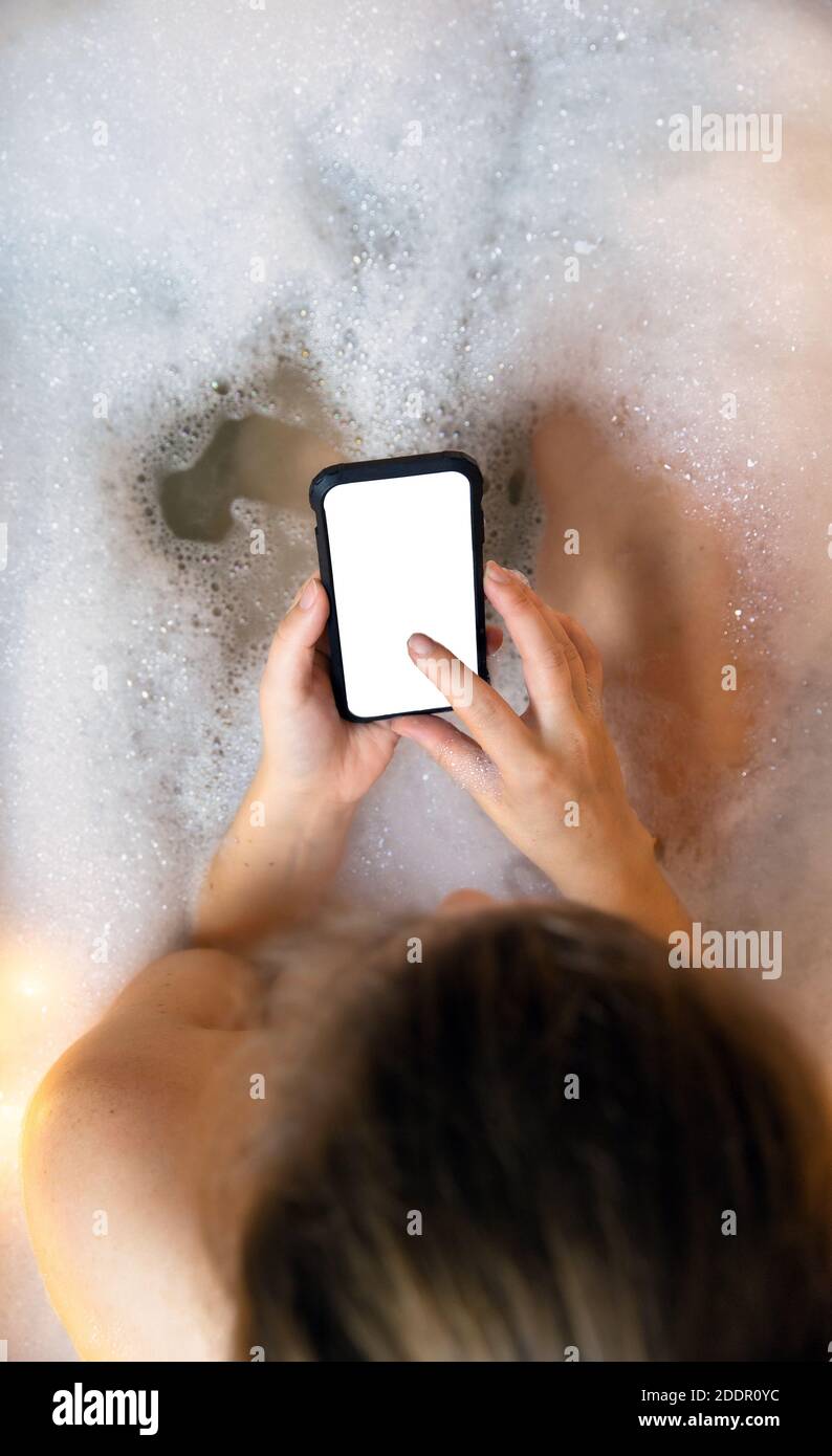 young female holding blank mobile phone, smart phone in bathtub with