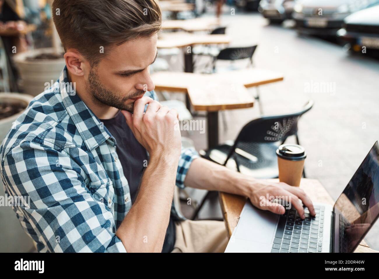 Happy young man working on laptop computer while sitting at sidewalk cafe Stock Photo