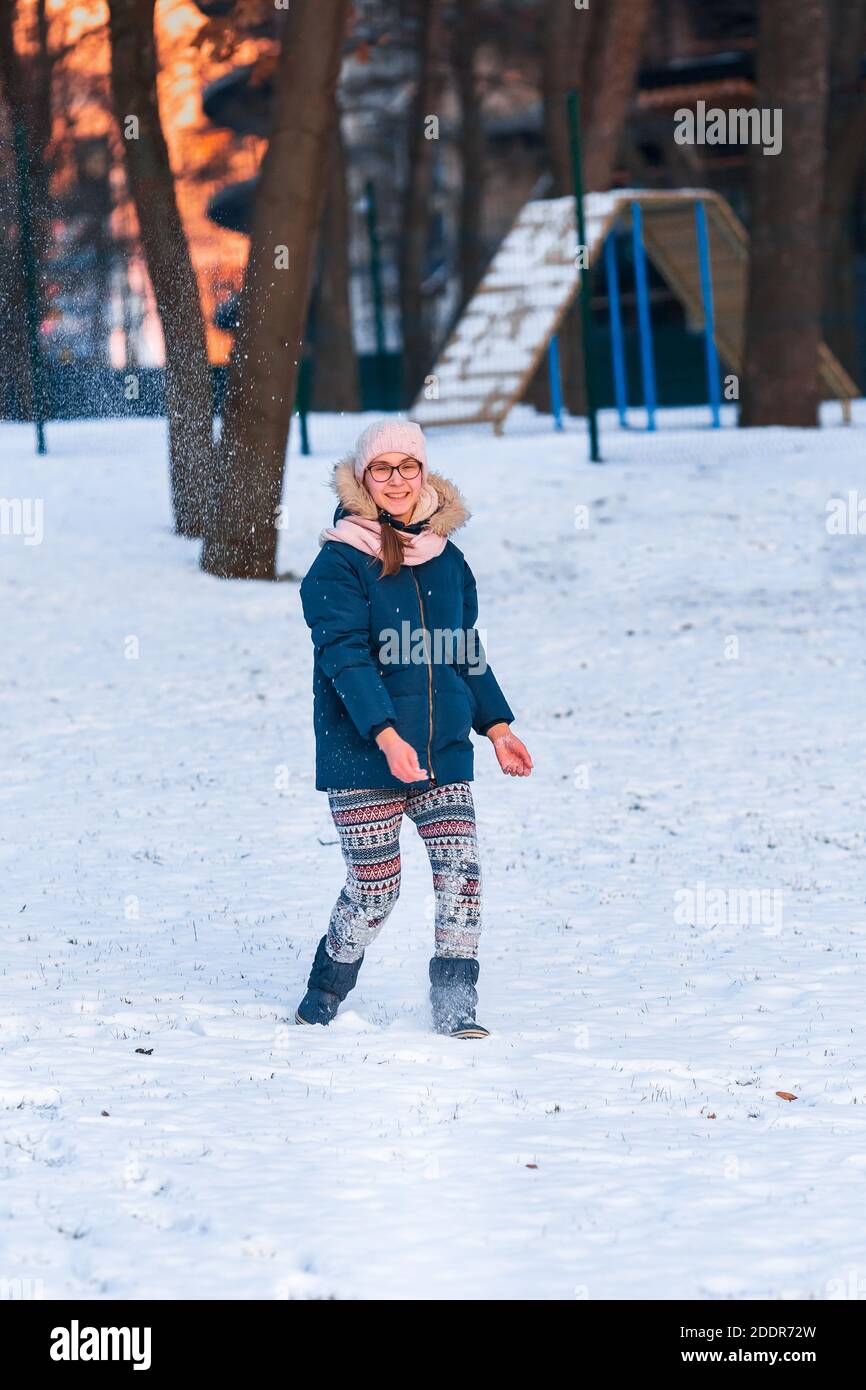 Happy teenage girl having a snowball fight, ready to throw a snowball, playing snowballs in winter park Stock Photo