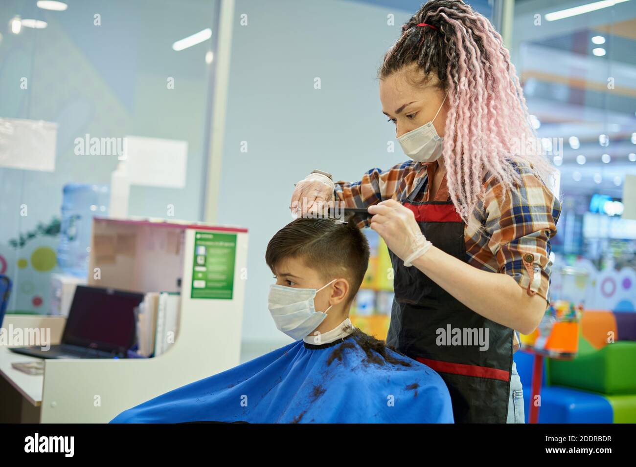 Caucasian white woman in face mask makes haircut to teenager in barbershop Stock Photo