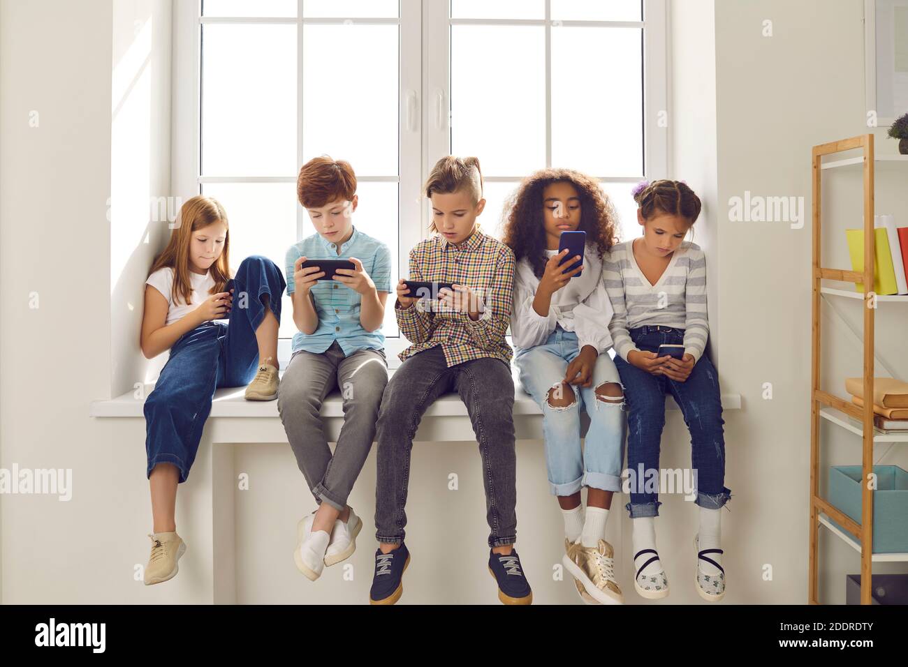 Children of different nationalities play online games or read social networks on mobile phones. Stock Photo