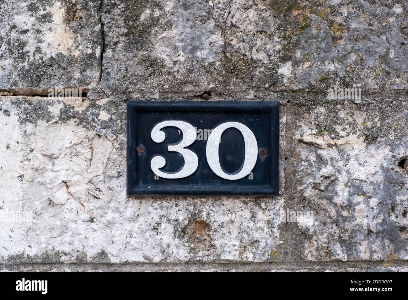 Street number thirty. Digit 30 white color on metal vintage plate mounted on stone wall. Traditional house address Stock Photo