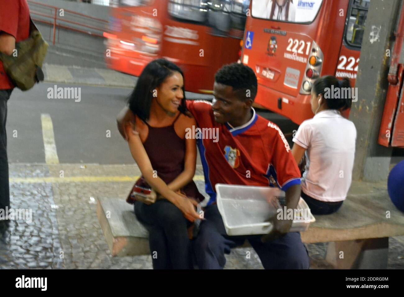 Couple of lovers, couple of students looking at each other and laughing, waiting for a bus, at a bus stop, company bus fund, Brazil, South America Stock Photo