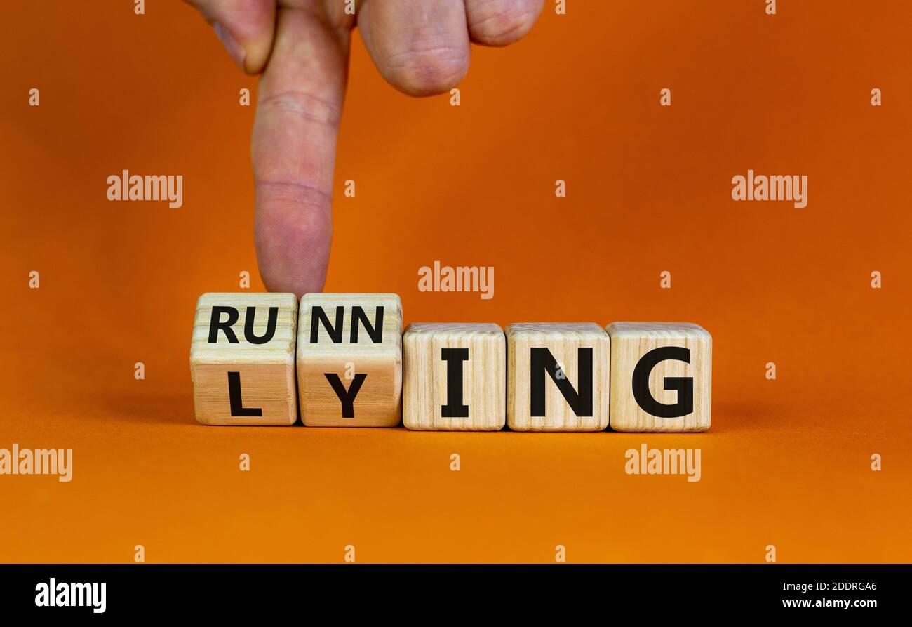 Lying or running. Hand is turning cubes and changes the word 'lying' to 'running'. Beautiful orange background. Lifestyle and motivational concept, co Stock Photo
