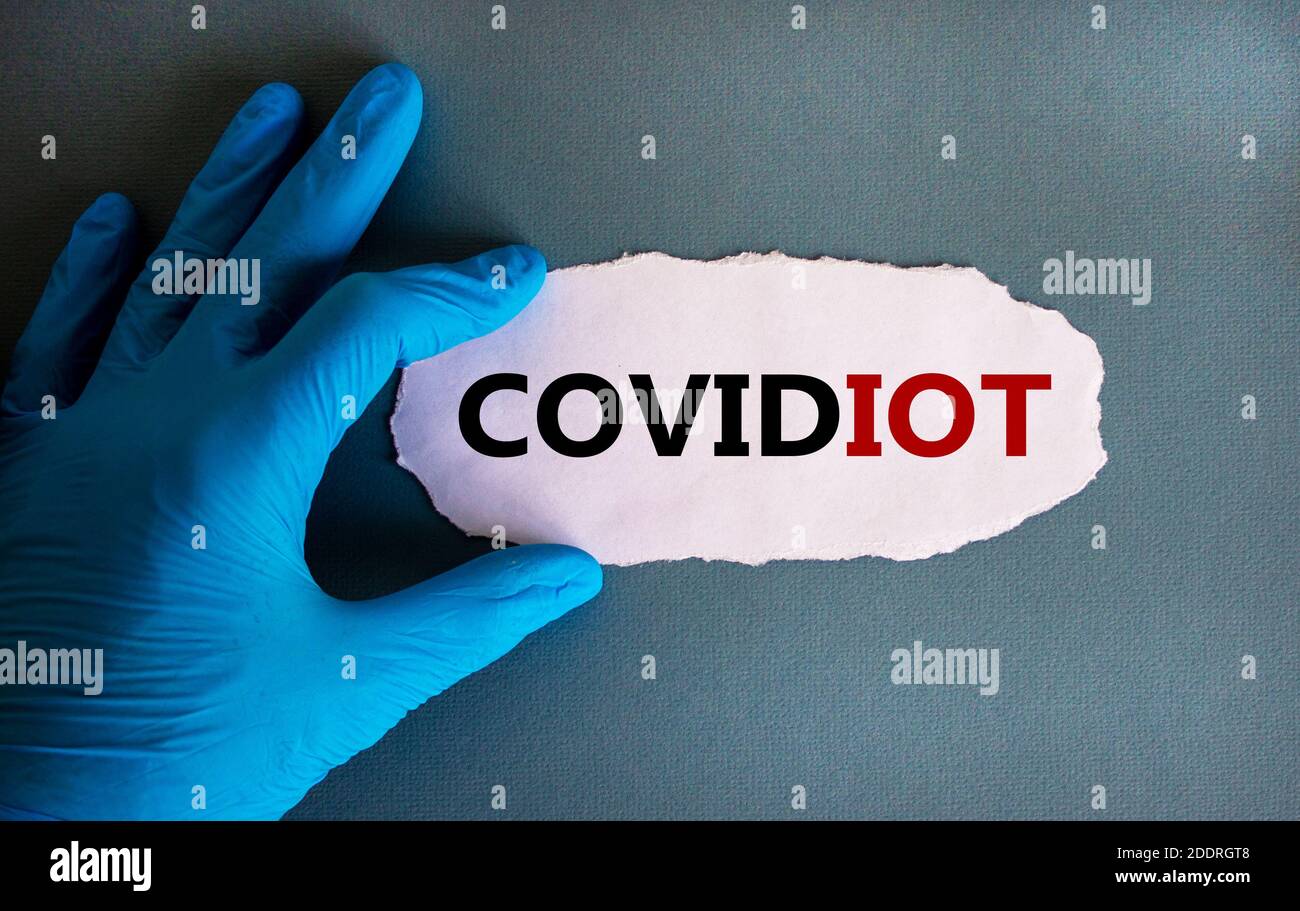 Stop covidiot. Hand in blue glove with white paper. Concept word 'covidiot'. Medical and covid-19 pandemic concept. Copy space, beautiful blue backgro Stock Photo
