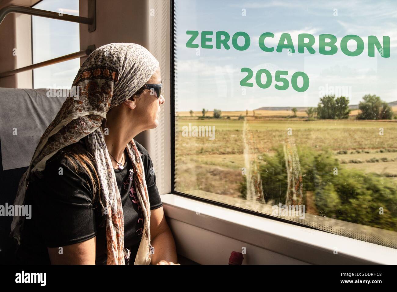 Woman looking out of train window with zero carbon 2050 on train window: global warming, climate change, air pollution..., concept Stock Photo